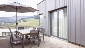 Une terrasse avec une table et des chaises, un grand parasol et une vue sur une rivière et des collines.
