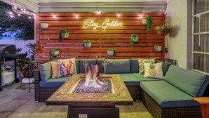 Un espace extérieur accueillant avec des sièges confortables, un foyer et des plantes en pot, le tout agrémenté d'une enseigne portant l'inscription « Stay Golden ».