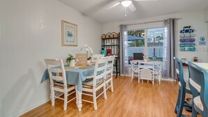 Un coin repas avec une table dressée pour quatre personnes, un ventilateur de plafond et une vue par la fenêtre.