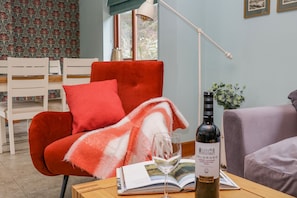 Una habitación acogedora con una silla roja, una mesa con una botella de vino y una copa, y un libro.