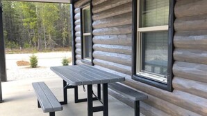 Une cabane en rondins dotée d’un patio couvert comprenant deux tables de pique-nique et un élément décoratif en pierre.