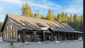 Une cabane en rondins dotée d’une grande véranda, d’un barbecue et d’une allée en gravier.