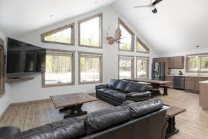 A spacious living area with a large leather sofa, a wooden table, and a flat-screen TV mounted on the wall. - Antler Ridge Cabin Rental - Pet Friendly! (Valemount)
