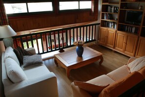 Uma sala de estar com corrimão de madeira, um sofá, uma mesa de centro e uma estante de livros.