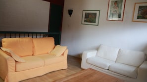 Dois sofás, um laranja e um branco, numa sala com parede de tijolos e quadros pendurados.