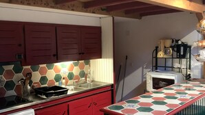A compact kitchen with red cabinets, a tiled backsplash, a built-in washing machine, and a microwave.