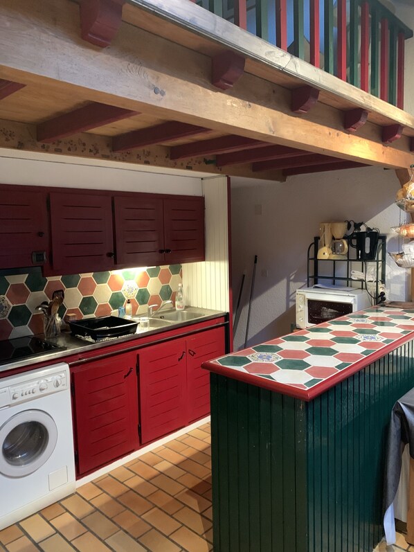 Cozinha compacta com armários vermelhos, painel de azulejos, máquina de lavar embutida e micro-ondas.