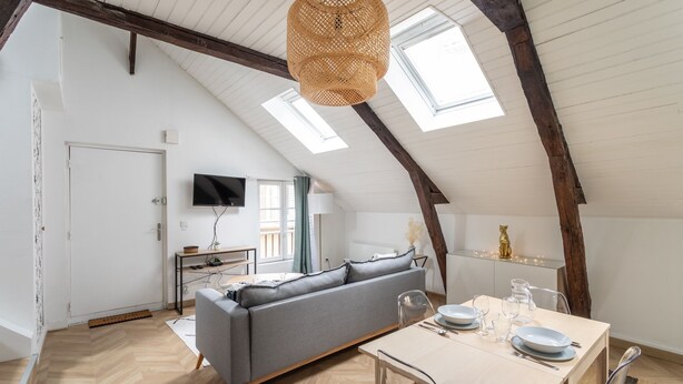 A loft-style room with a sofa, dining table, and a TV mounted on the wall. - LE PETIT MARIUS - Cocon au cœur du centre-ville historique (Rennes)
