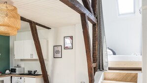 A modern loft with exposed wooden beams, a kitchenette, a sofa, and a staircase leading to an upper level. - LE PETIT MARIUS - Cocon au cœur du centre-ville historique (Rennes)