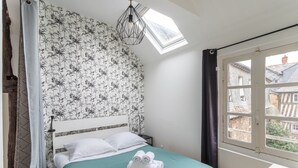A bedroom with a bed, a skylight, a window, and a view of buildings outside. - LE PETIT MARIUS - Cocon au cœur du centre-ville historique (Rennes)