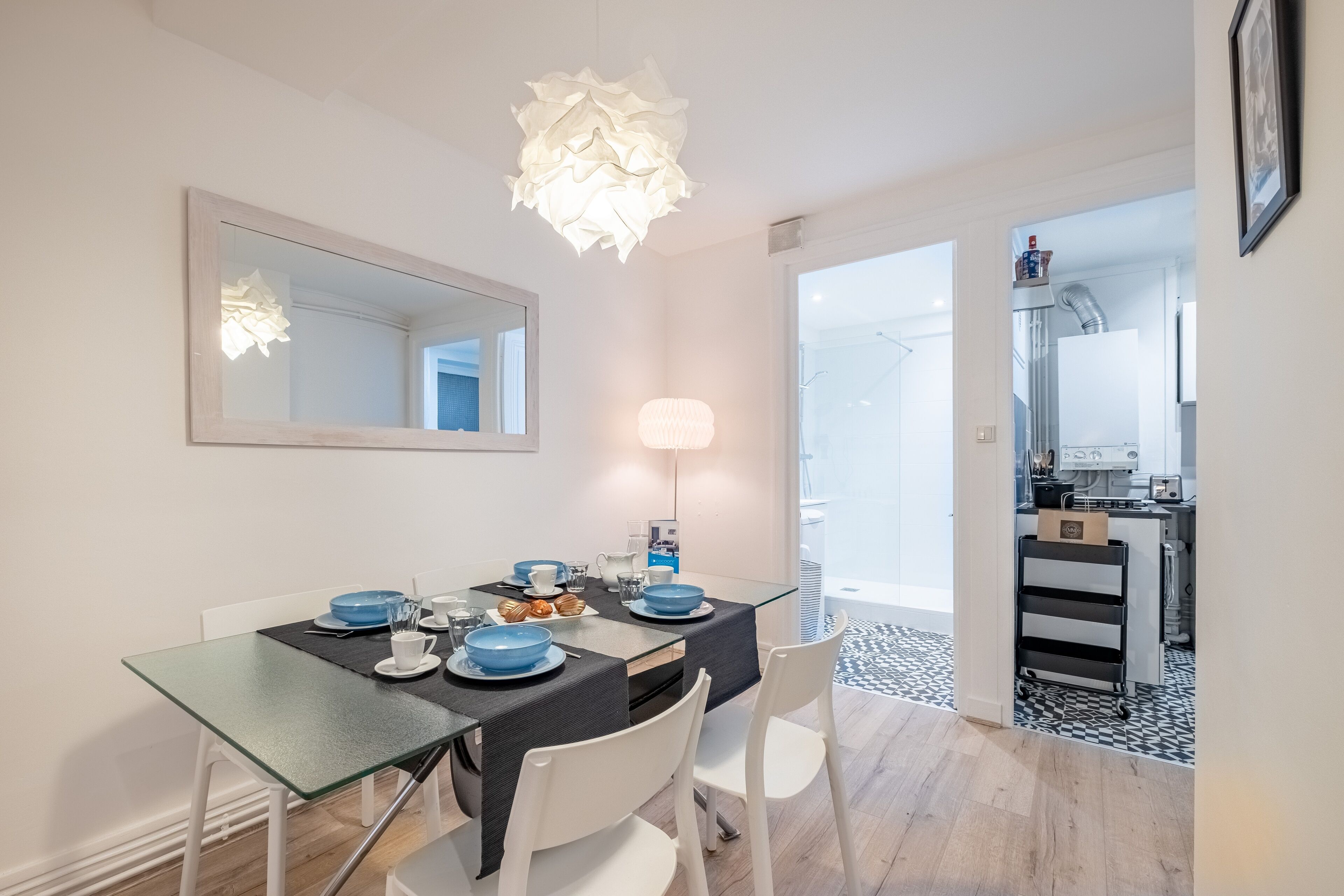 A modern dining area with a glass table, white chairs, and a black table runner. A large mirror hangs on the wall above the table.