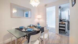 A modern dining area with a glass table, white chairs, and a black table runner. A large mirror hangs on the wall above the table. - Isadora - Ravissant T2 au coeur de Lyon (Lyon)