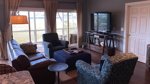 Ein Wohnzimmer mit Sofa, Sessel, Hocker und einem Fernseher auf einem Schrank.