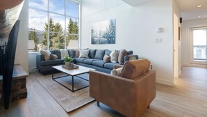 Een moderne woonkamer met een groot raam, een grijze bank, een bruine fauteuil en een salontafel.