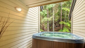 Een bubbelbad in een kamer met houten wanden en een raam met uitzicht op een bos.