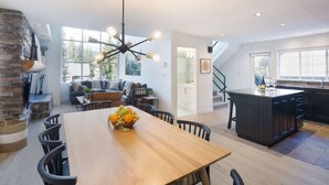 Een moderne keuken met een centraal eiland, een eetgedeelte met een houten tafel en stoelen, en een accentmuur van steen.