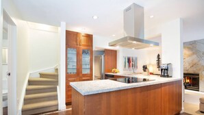 A modern kitchen with a central island, wooden cabinetry, and a built-in stove. - Prime Location: 4-Bedroom Chalet Style Home (Whistler)