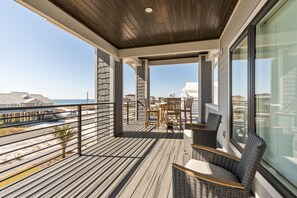 A covered outdoor balcony with a wooden floor, wicker furniture, and a view of the beach and ocean. - Gulf Sound-Gulf & Sound view private home w/heated pool (Navarre)