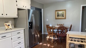 A kitchen with white cabinets, a stainless steel refrigerator, wooden dining table, and chairs.