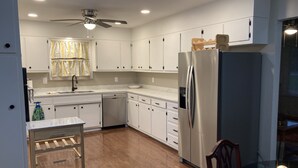 A modern kitchen with white cabinets, a stainless steel refrigerator, a dishwasher, and a ceiling fan.