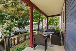 A covered porch with wicker furniture, a view of the street, and a wooden fence. - Nest on Vestry: Spacious Historical Home w/ Jacuzzi & Pool Table (Cleveland)
