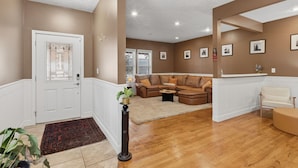 A spacious living room with a brown leather sectional sofa, a white armchair, and a wooden floor.