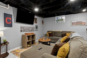 A living room with a sectional sofa, a coffee table, and a TV mounted on the wall. - Nest on Vestry: Spacious Historical Home w/ Jacuzzi & Pool Table (Cleveland)