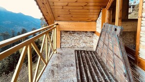 A wooden balcony with a bench, stone wall, and a view of mountains. - An artsy and peaceful mountain stay located in an offbeat village of Shoja (Banjar)