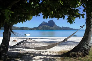 A hammock under a tree on a beach with a boat in the water and a mountain in the background. - Gorgeous Over Water Bungalow in Bora Bora. Perfect spot Honeymooners & Families (Bora-Bora)
