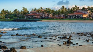 A beachfront hotel with multiple buildings, palm trees, and a rocky shoreline. - Waiohai Beach Club - Island View (Kauai)