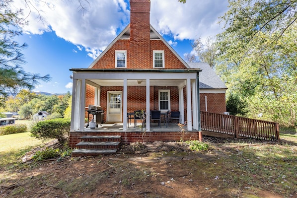 A brick house with a porch, a chimney, and a fenced yard.