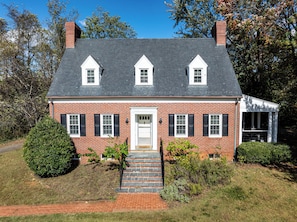 A brick house with a white door, two dormer windows, and a covered porch.