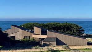 A modern building with a sloped roof, situated near a body of water and surrounded by greenery.