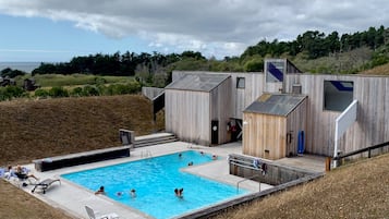 Ein Poolbereich mit Holzterrasse, Liegestühlen und einem kleinen Gebäudebau.