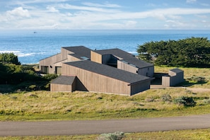 A modern building with a flat roof, situated on a grassy hill overlooking the ocean.