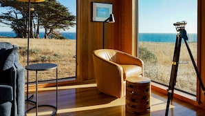 A room with wooden walls and large windows, a tripod, a chair, a small table, and a floor lamp.
