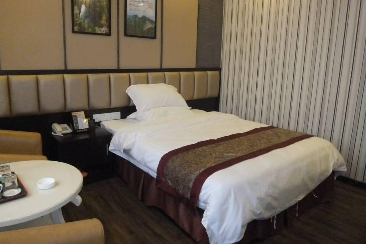 A hotel room with a bed, a bedside table with a phone, a small table with a tray of items, and a chair.