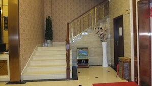 Un vestíbulo de hotel con una escalera de mármol, un mostrador de recepción y un jarrón grande con flores.