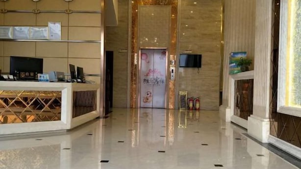 Un vestíbulo de hotel con una recepción, un televisor montado en la pared y un piso limpio y brillante.