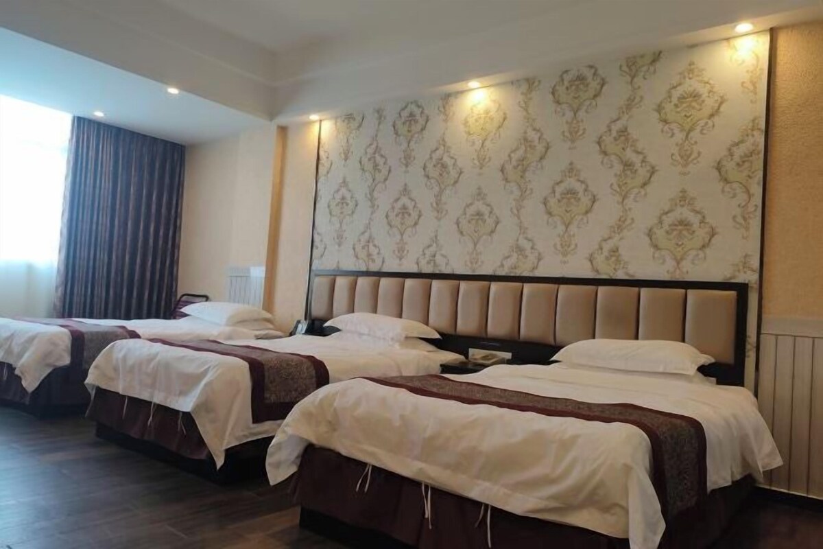 A hotel room with two beds, a large patterned wall, and a window with curtains.