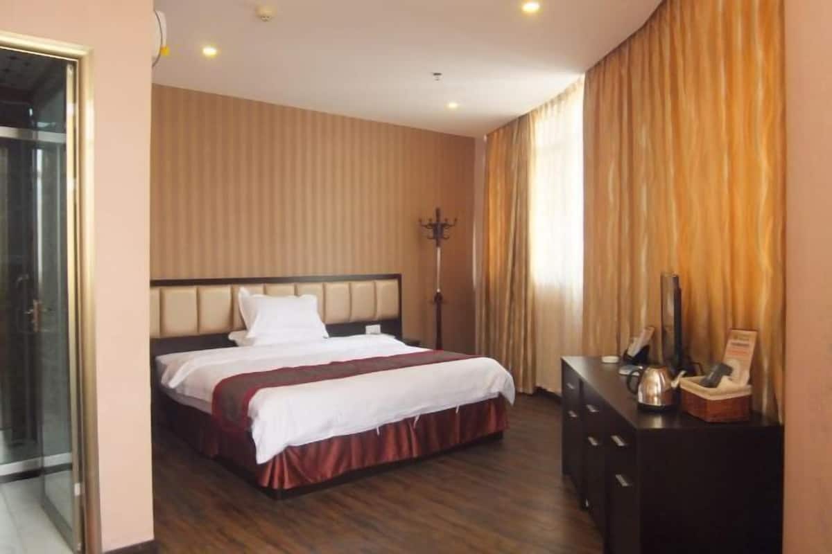 A hotel room with a bed, a dresser, a mirror, a coat rack, and a door leading to a bathroom.