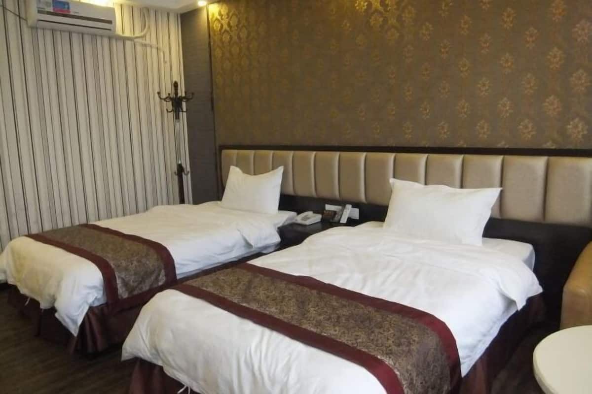 A hotel room with two beds, a headboard, a bedside table, and a wall-mounted air conditioning unit.