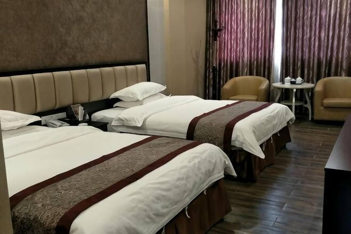 A hotel room with two beds, a small table, a chair, and a window with curtains.