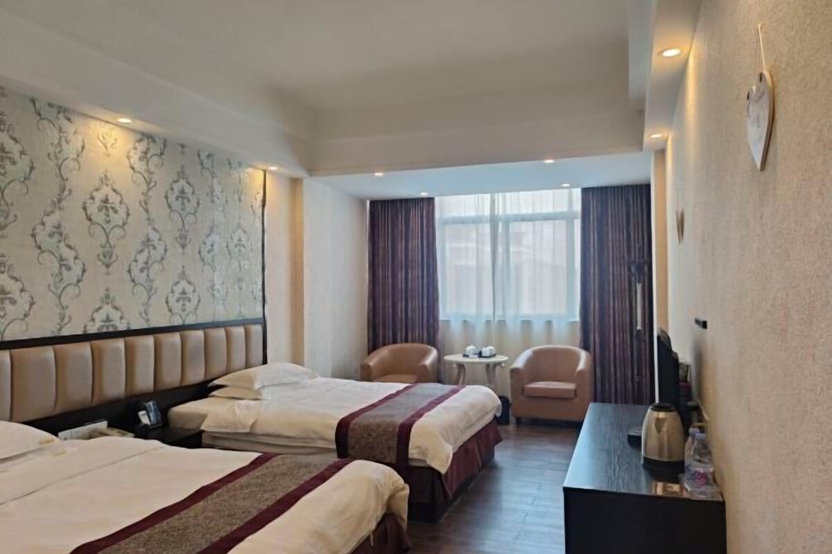 A hotel room with two beds, a desk, a chair, and a small table.