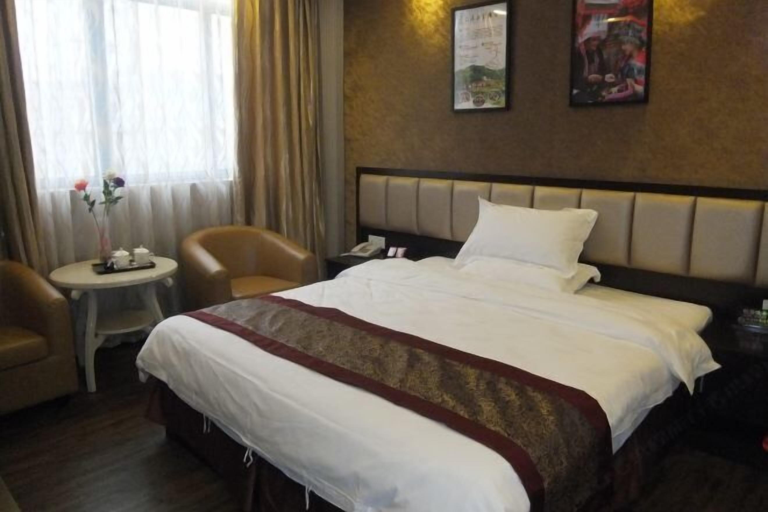 Una habitación de hotel con una cama, una mesita redonda pequeña, dos sillas y una mesita de noche con una lámpara.