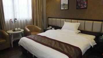 Una habitación de hotel con una cama, una mesita redonda pequeña, dos sillas y una mesita de noche con una lámpara.