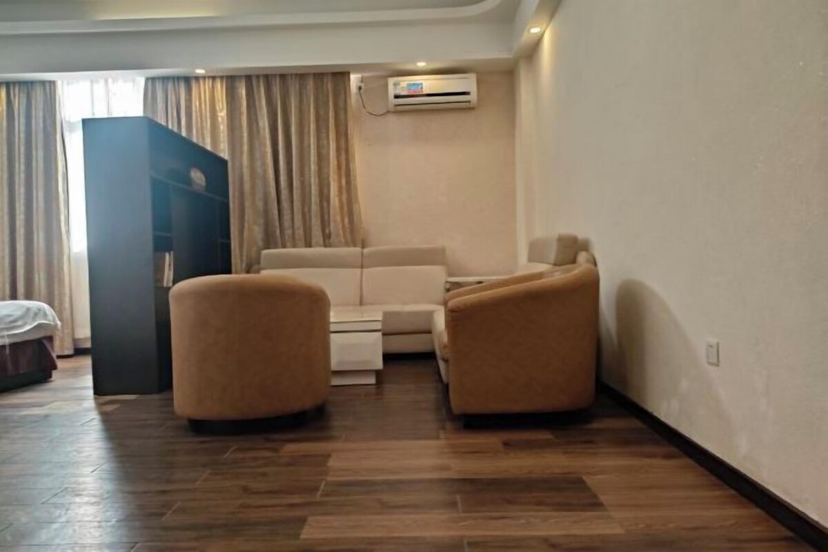 A hotel room with a sofa, two armchairs, a wooden floor, and a wardrobe.
