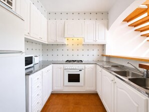 Una cocina compacta con muebles blancos, estufa a gas, microondas y pileta.