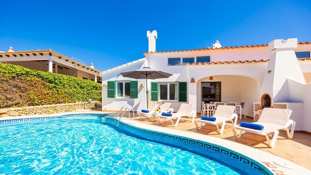 A poolside area with lounge chairs, a pool, and a building with a white facade and green shutters.