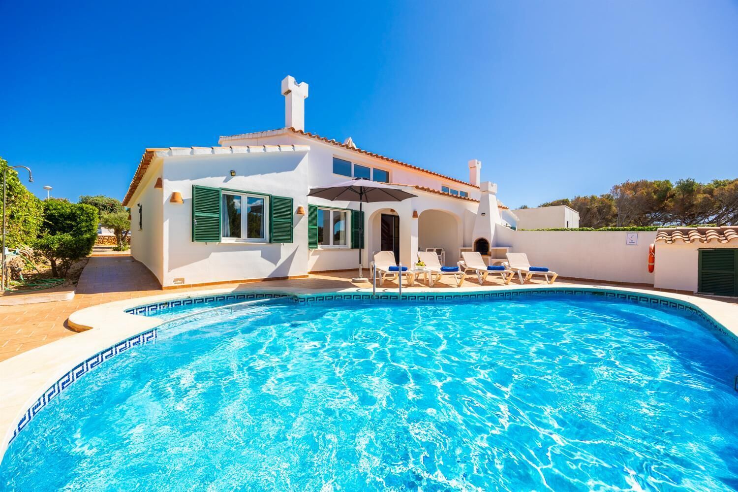 A white villa with a swimming pool, green shutters, and a tiled roof.